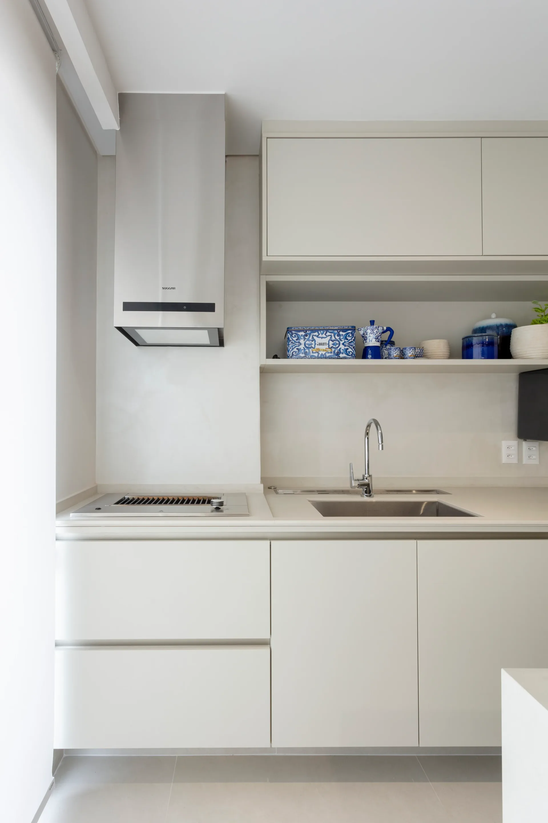 Cozinha compacta branca com cooktop, cuba e nicho aberto com louças azuis, coifa retrátil embutida