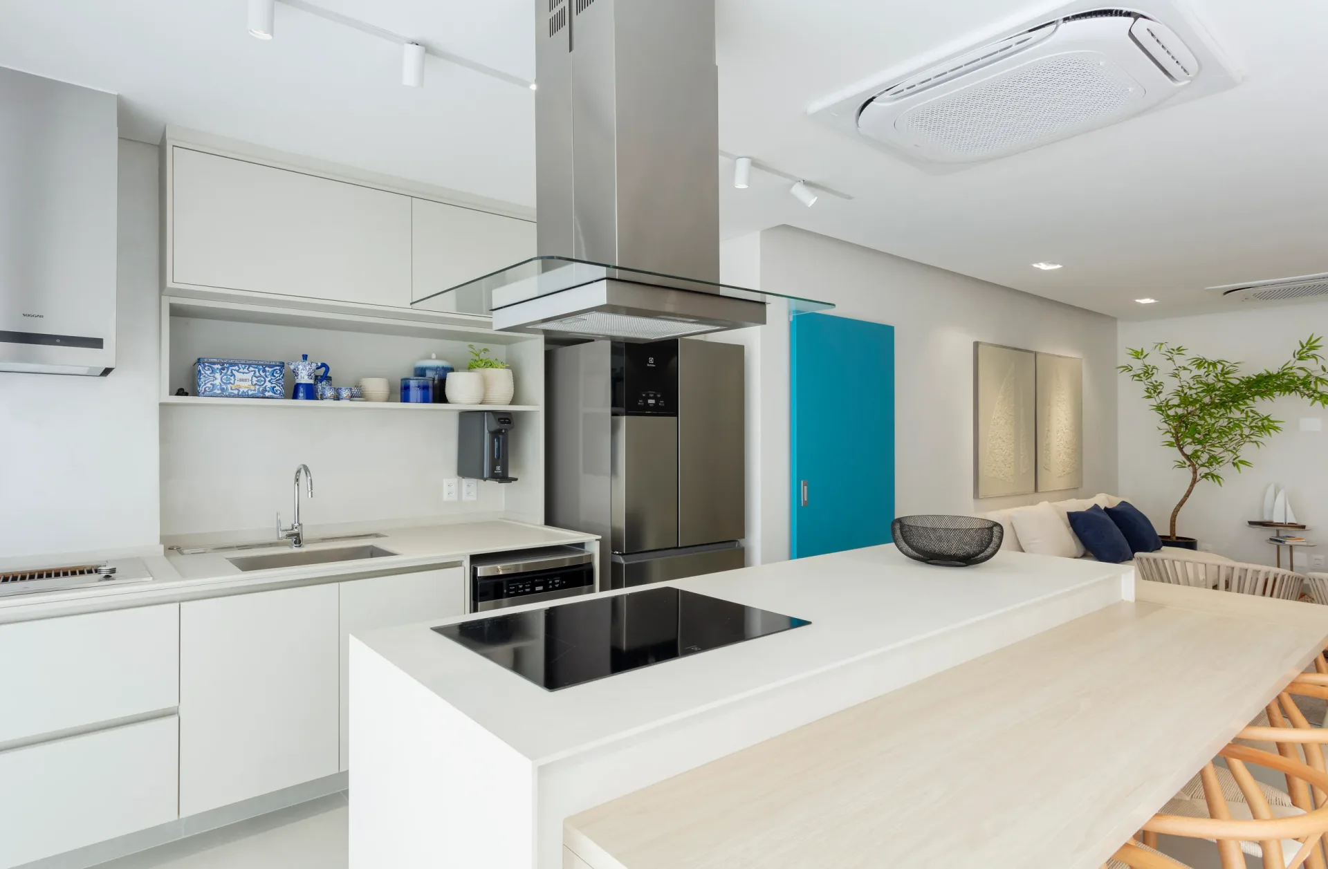 Cozinha branca com ilha de cooktop, coifa de inox suspensa e bancada de madeira clara ao lado