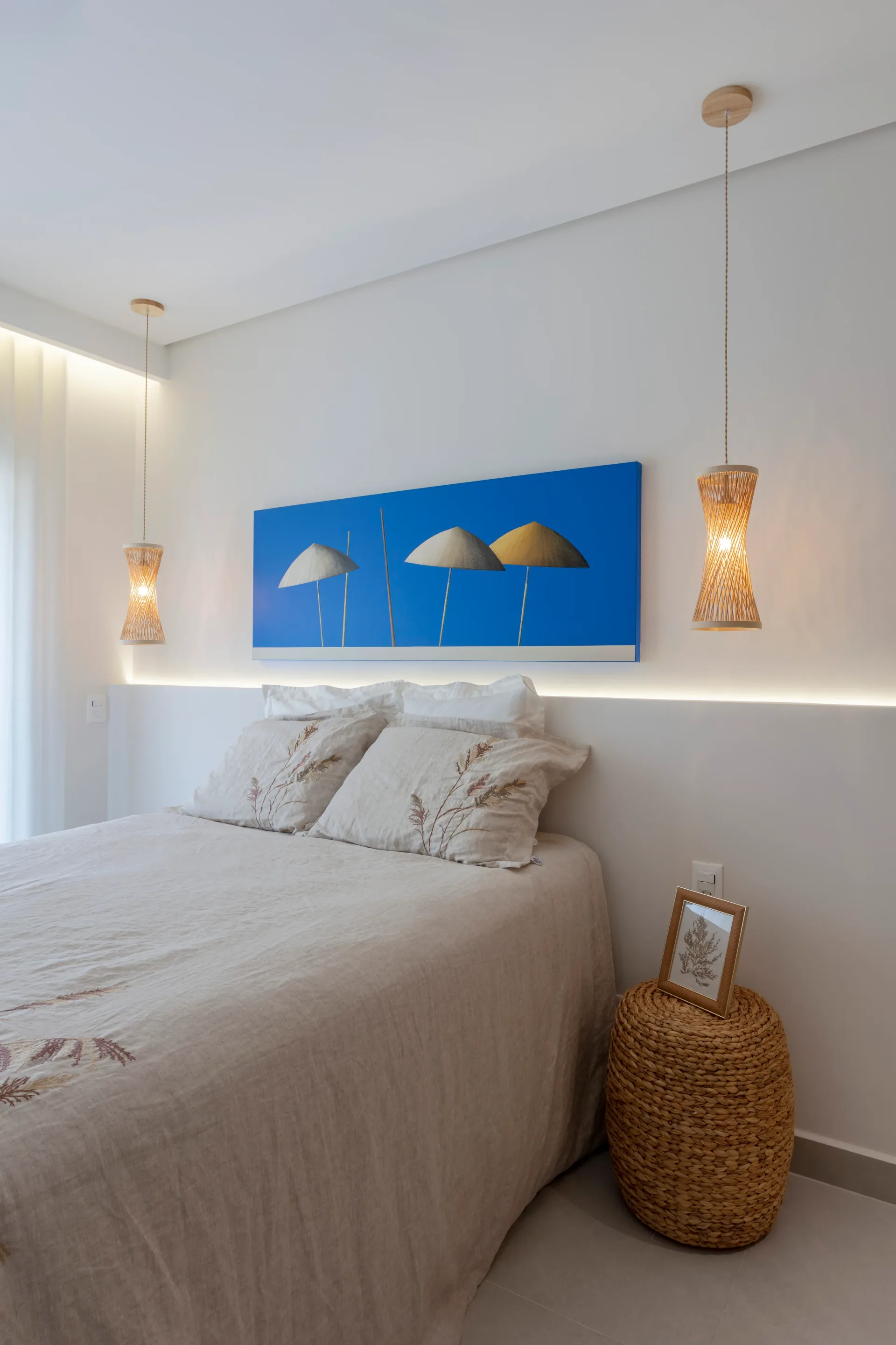 Quarto de casal com cabeceira contínua que se estende como bancada lateral, quadro azul e pendentes de fibra